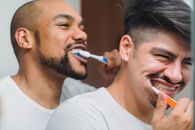 两个男人微笑着，愉快地一起刷牙，享受早晨的例行公事，促进健康和卫生