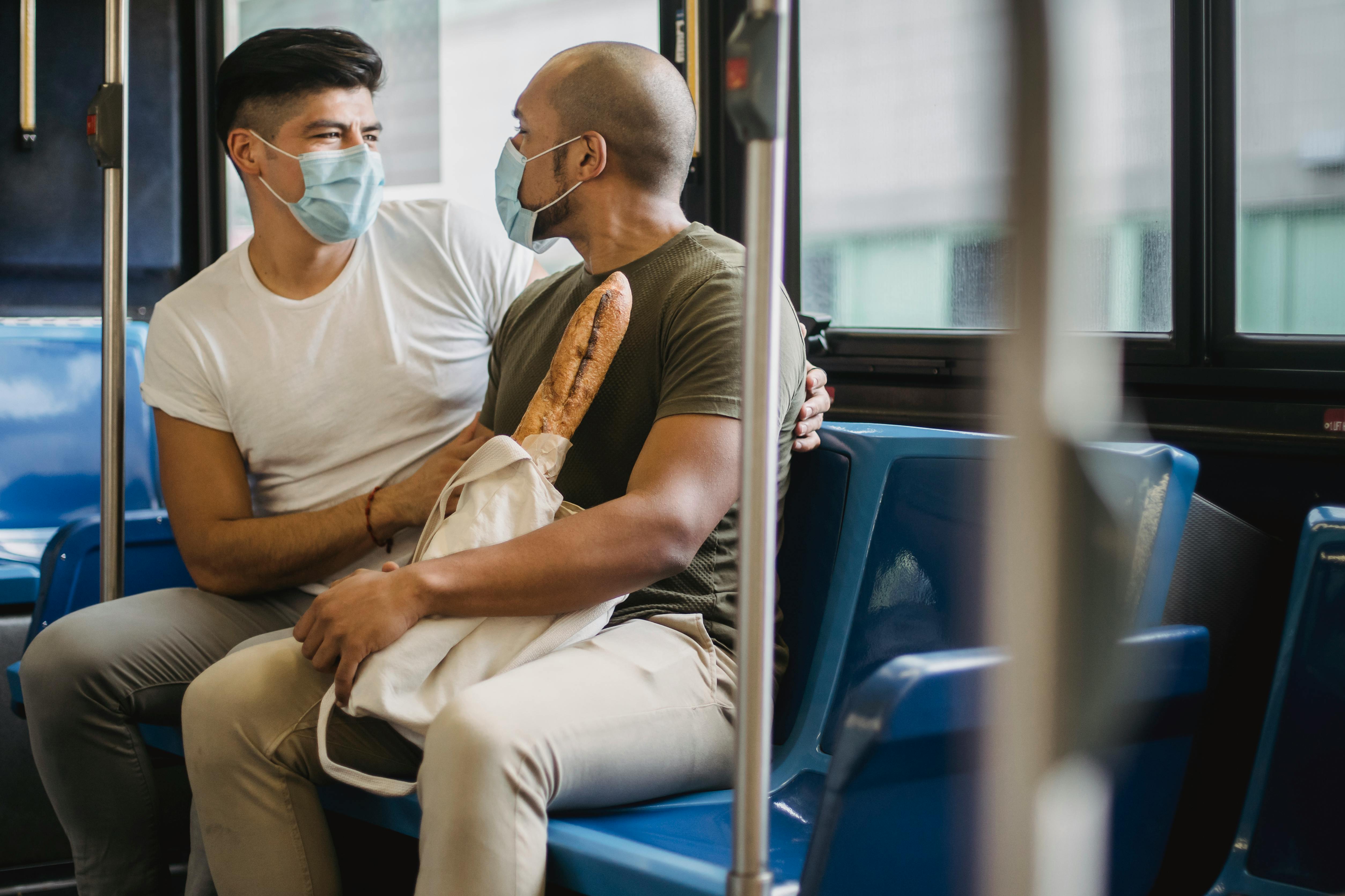 two men wearing face masks sitting in public transportation