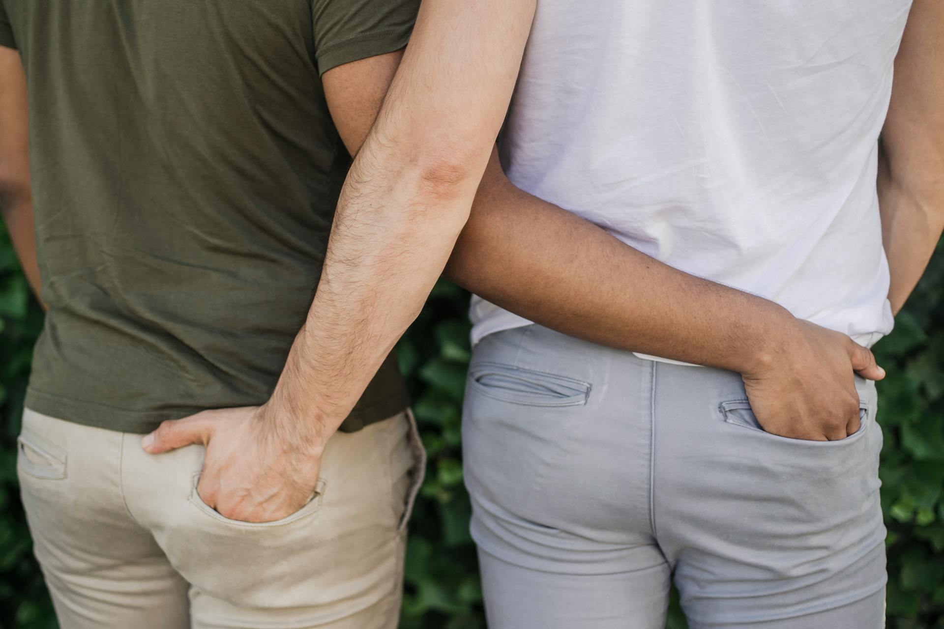 Interracial gay couple holding hands, symbolizing love and togetherness. Back view outdoors on a sunny day.