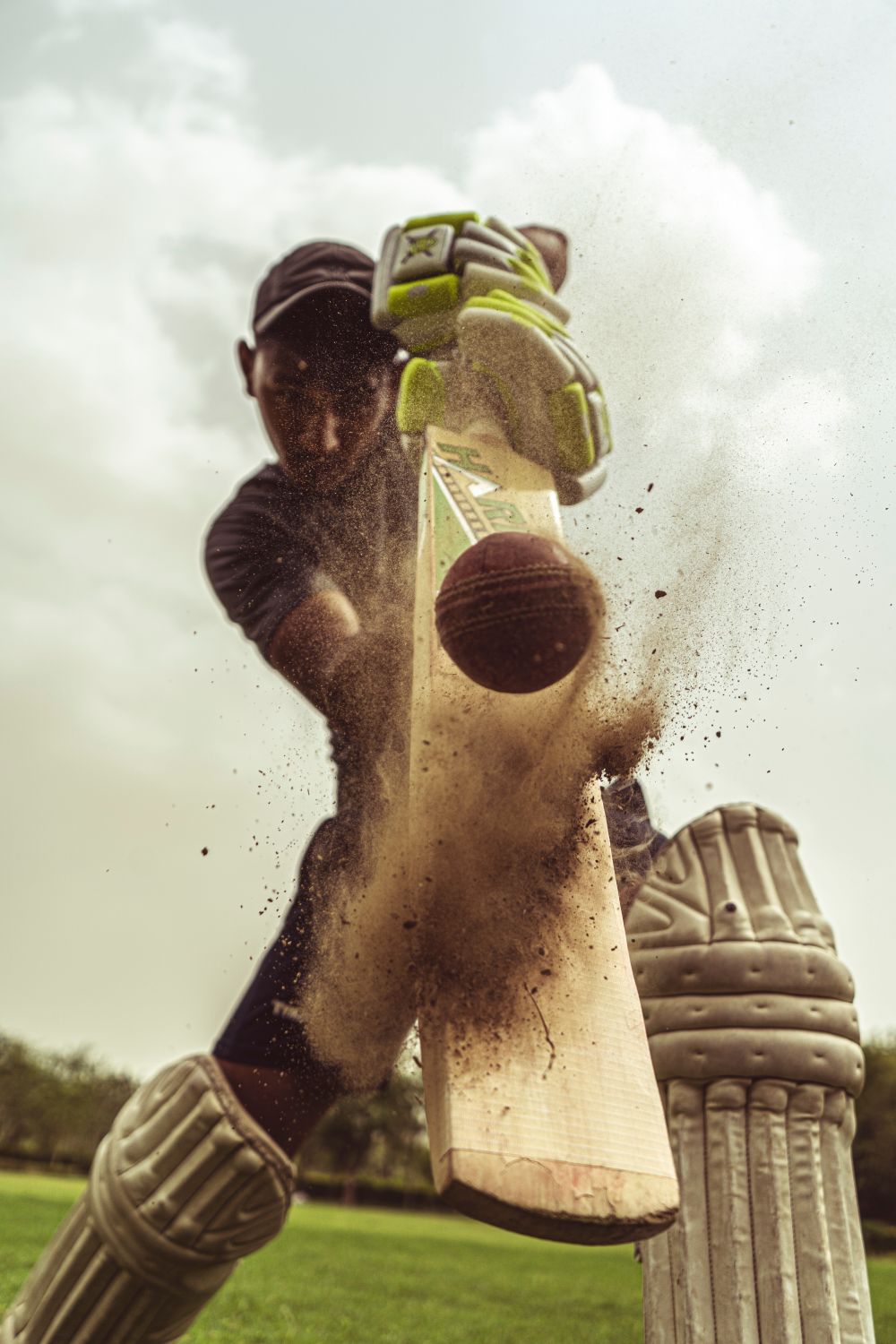 Low-angle action shot of a cricketer striking the ball, dust kicked up around the pitch