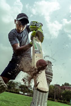 A focused cricket player striking a ball with dramatic effect outdoors.