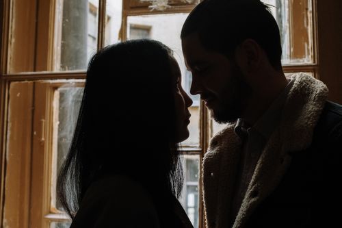 Free A romantic silhouette of a couple facing each other in front of a window indoors. Stock Photo