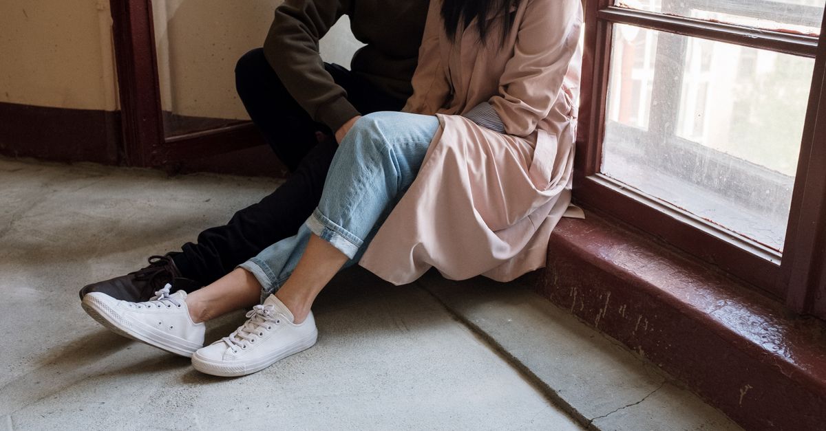A casual couple sitting on the stairs indoors by a window. Faceless and intimate setting.