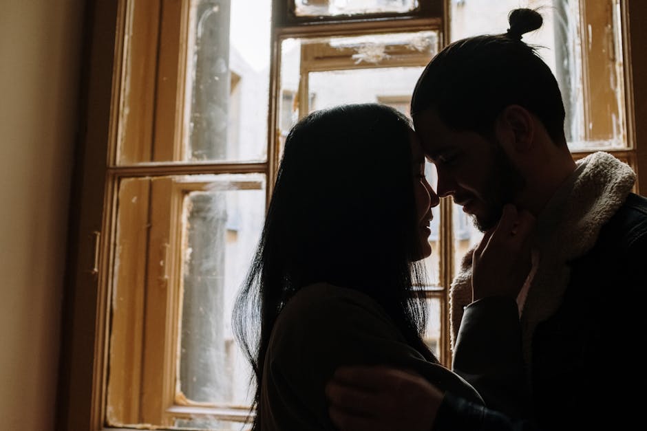 Silhouette of a couple embracing tenderly by a window, capturing a romantic moment.