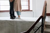 Woman in Brown Coat and Blue Denim Jeans Standing on Gray Concrete Staircase