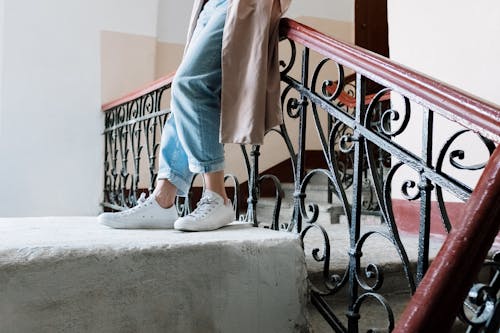 Person in Blue Pants and White Sneakers Standing on Gray Concrete Staircase