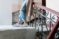 室内，一名女子穿着休闲牛仔裤和运动鞋，靠在古董楼梯的栏杆上