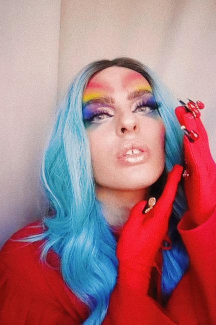 Dazzling portrait of a person with rainbow eyeshadow, blue hair, and red attire, exuding glamour.
