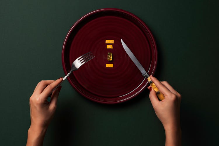 Person Holding A Fork And Knife With Gummy Bear And Sticker On Plate