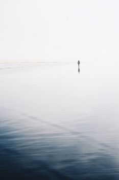 A lone figure walks along a serene Chilean beach, creating a minimalist seascape scene.