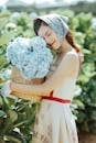 Side view of pleased Asian female gardener in headscarf standing with eyes closed near green bushes with flowers in wicker bucket in hands