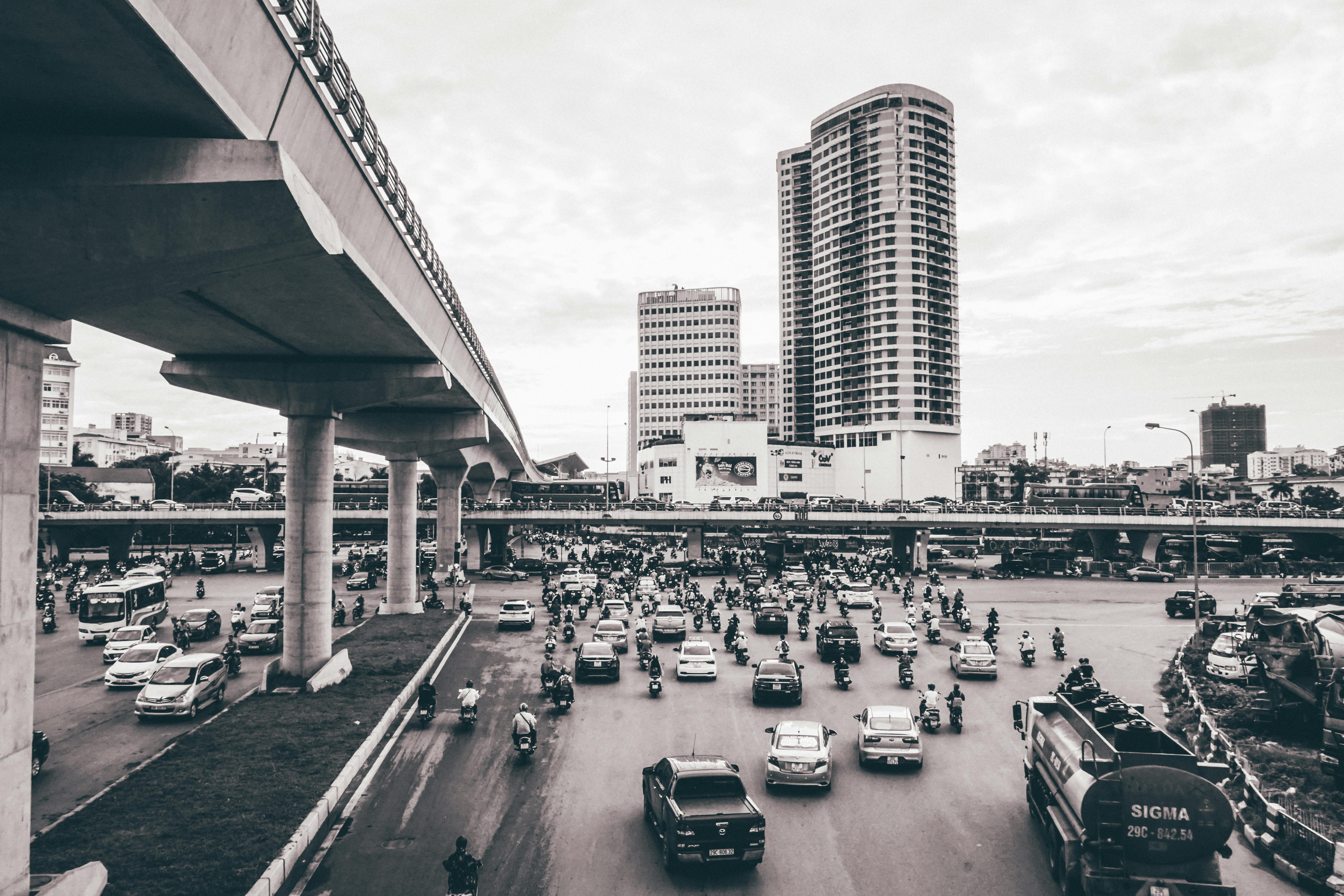 Aerial view of busy Hanoi intersection with cars and motorcycles amid towering skyscrapers.