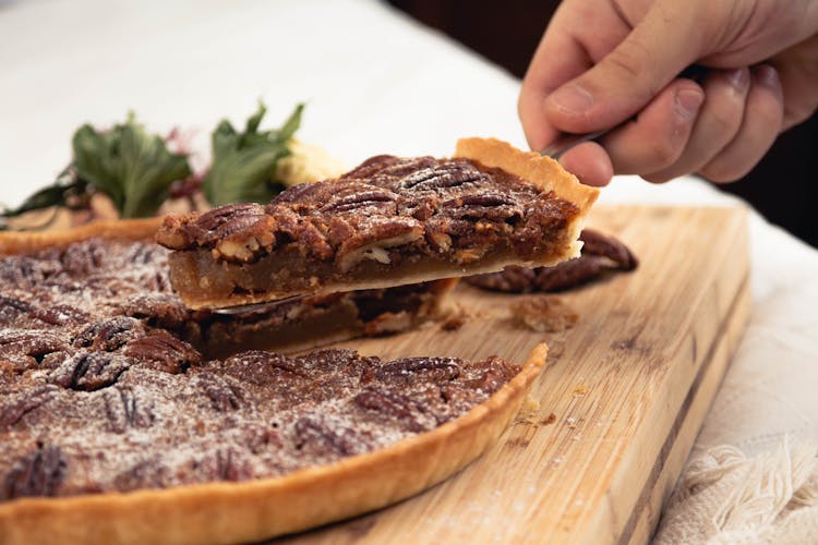 A Hand Holding A Sliced Of Pecan Pie