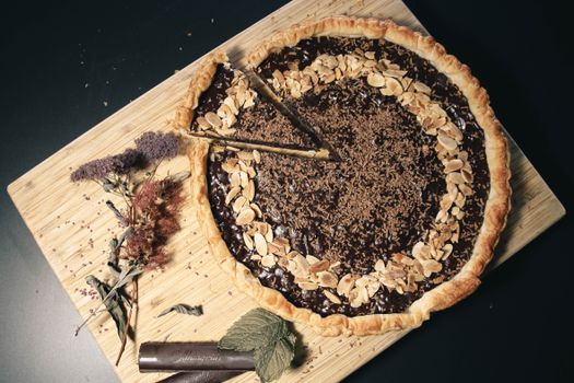 Elegant chocolate almond tart garnished with almonds, served on a wooden tray with decorative flowers.