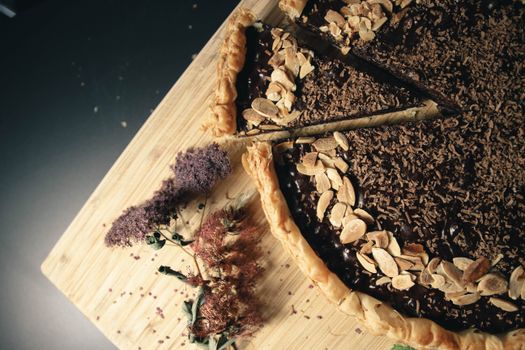 Delicious chocolate almond pie with slice cut, garnished with flowers on a wooden board.