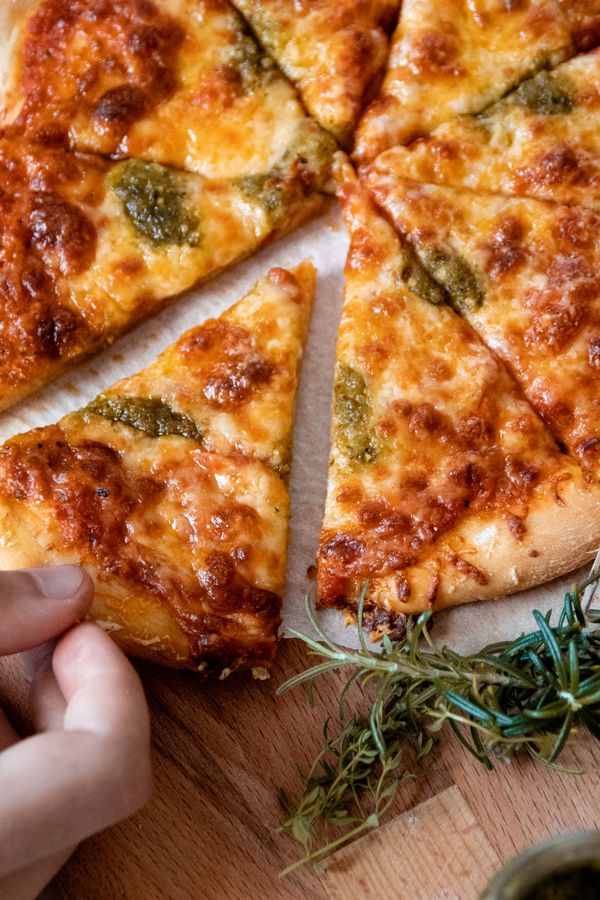 A hand holding a margherita pizza with pesto over a wooden board — photo by Regina Ferraz on Pexels