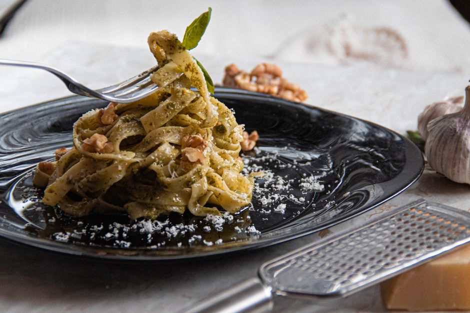 Indulge in homemade pesto pasta topped with parmesan and walnuts, beautifully plated.
