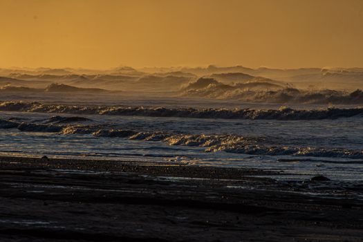 Captured at sunset, this image showcases dramatic ocean waves crashing against the seashore.