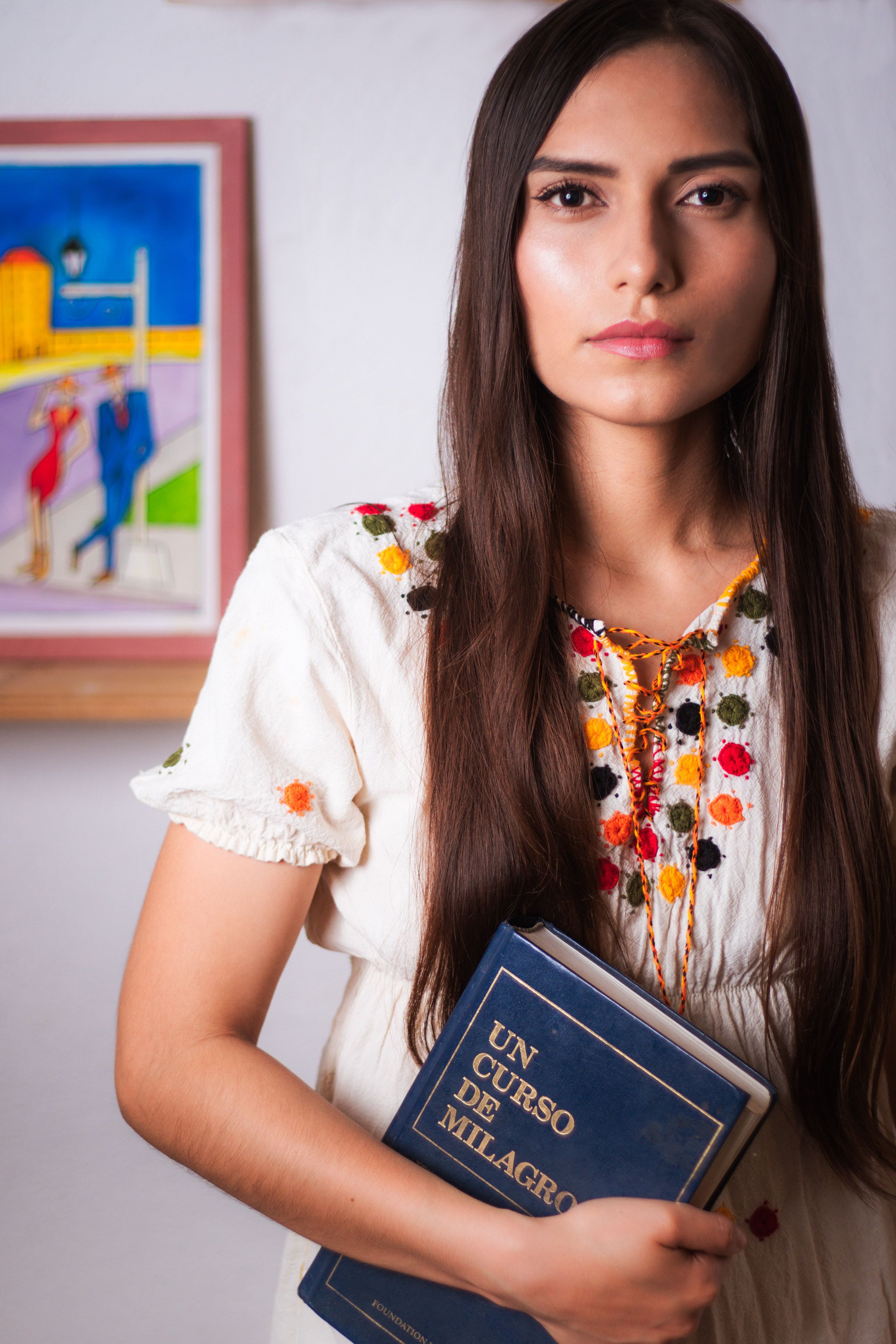 Serious woman in traditional attire with book 'Un Curso de Milagros' in Cancún, Mexico.