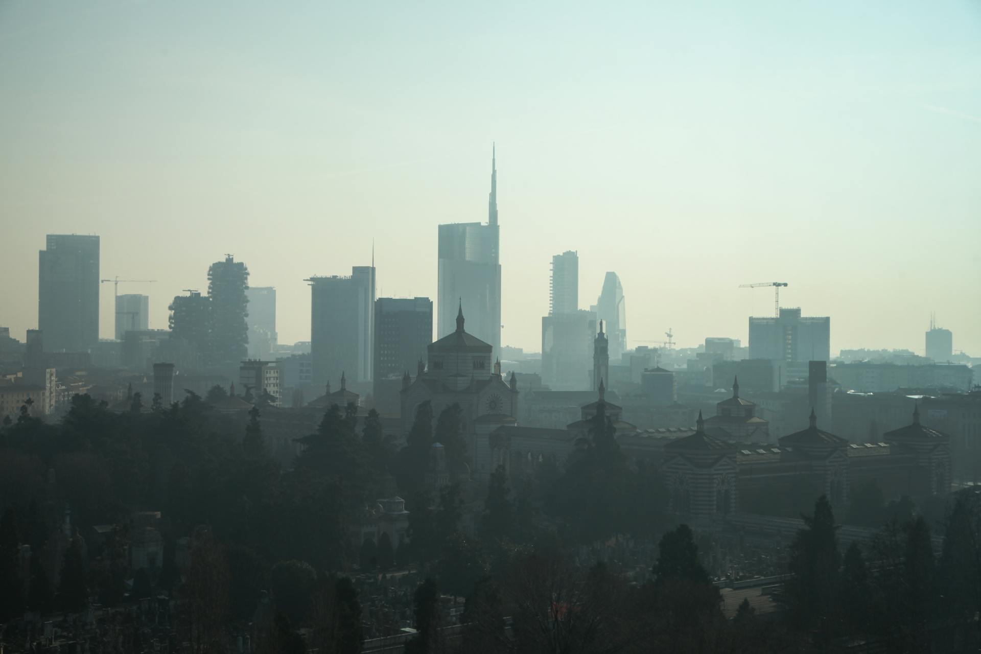 A foggy view of the Milan cityscape with modern skyscrapers and historic architecture.