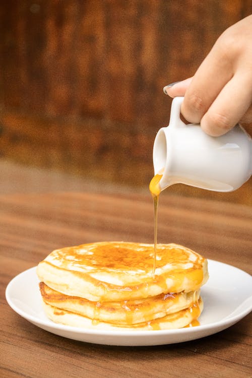 Person Pouring Brown Syrup on Pancakes 