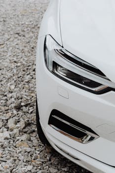 一辆白色汽车停在砾石上，其前灯和设计细节清晰可见
