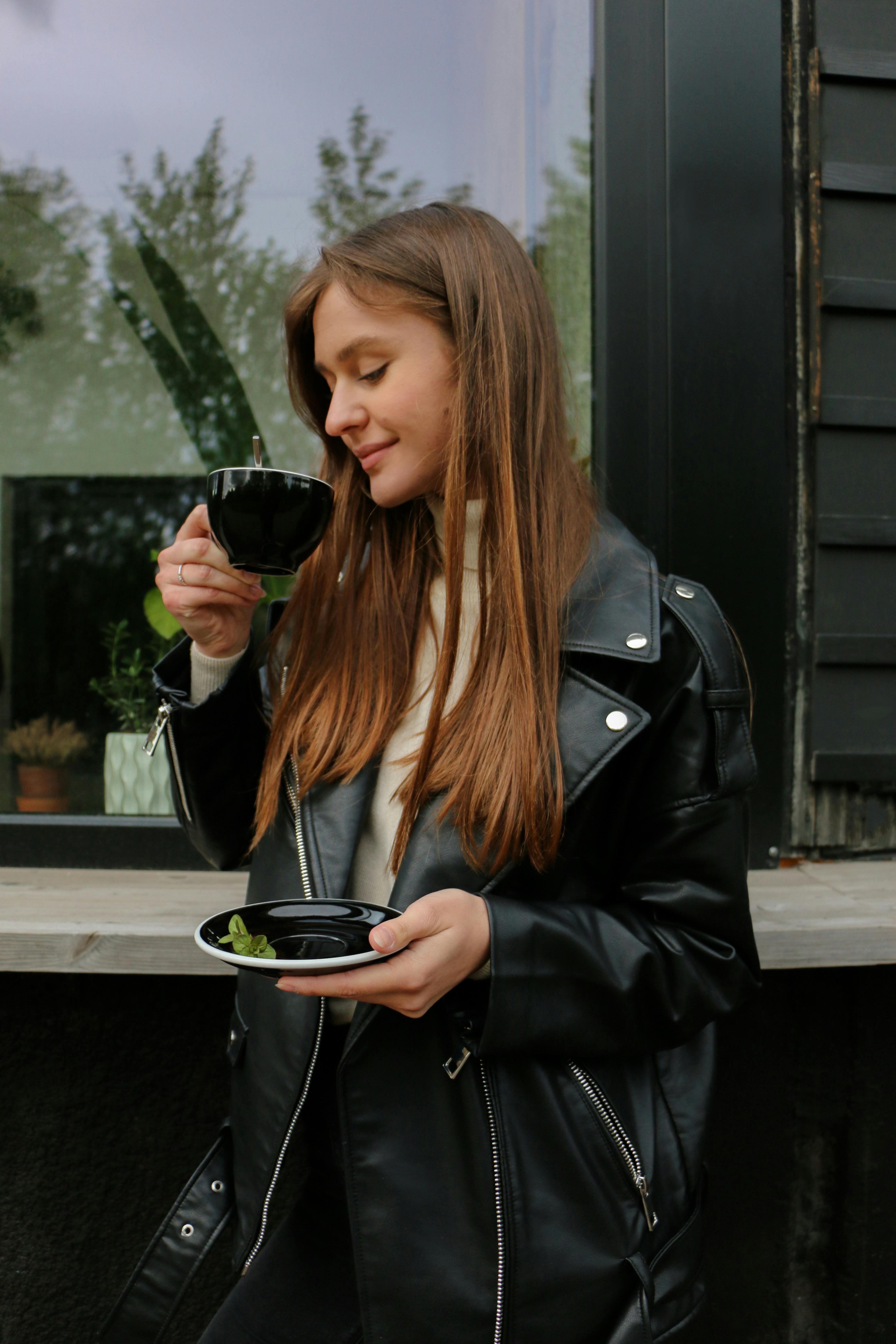 一位穿着黑色皮夹克的女子微笑着喝咖啡