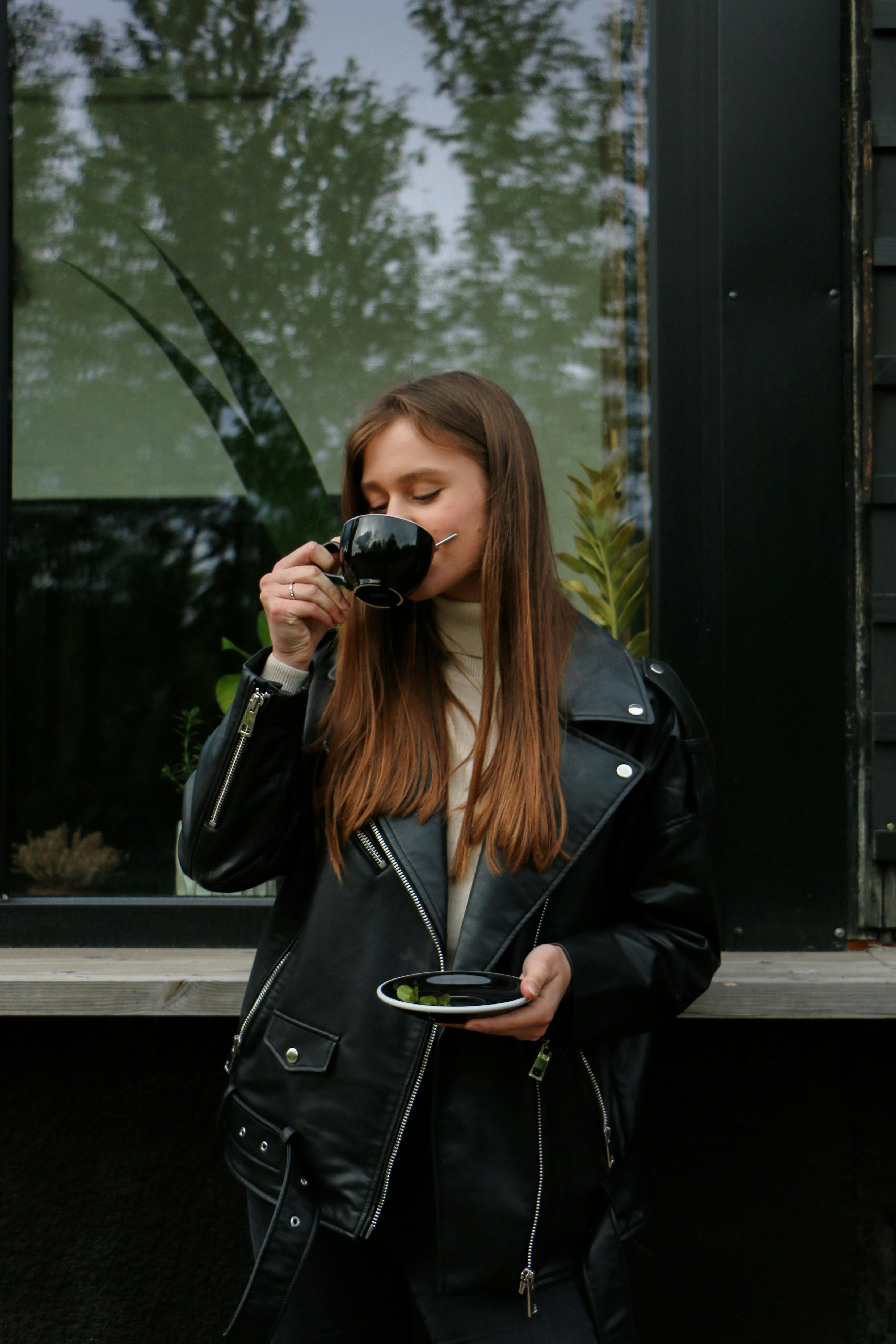 a woman in a black leather jacket drinking coffee