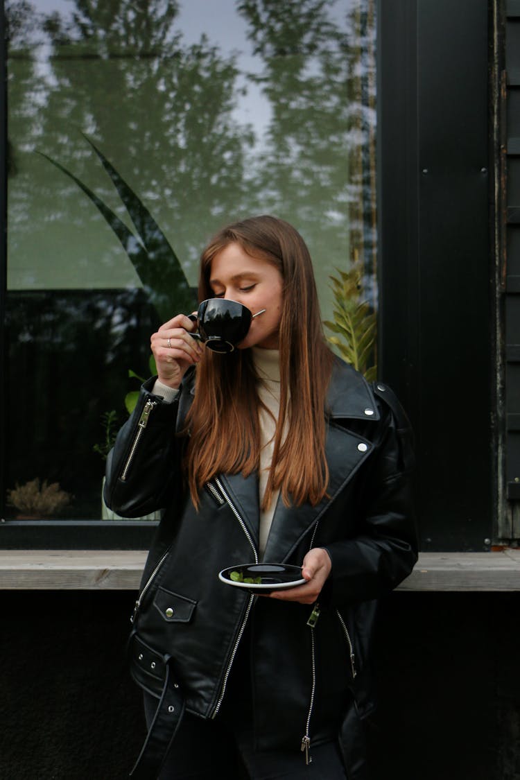 A Woman In A Black Leather Jacket Drinking Coffee