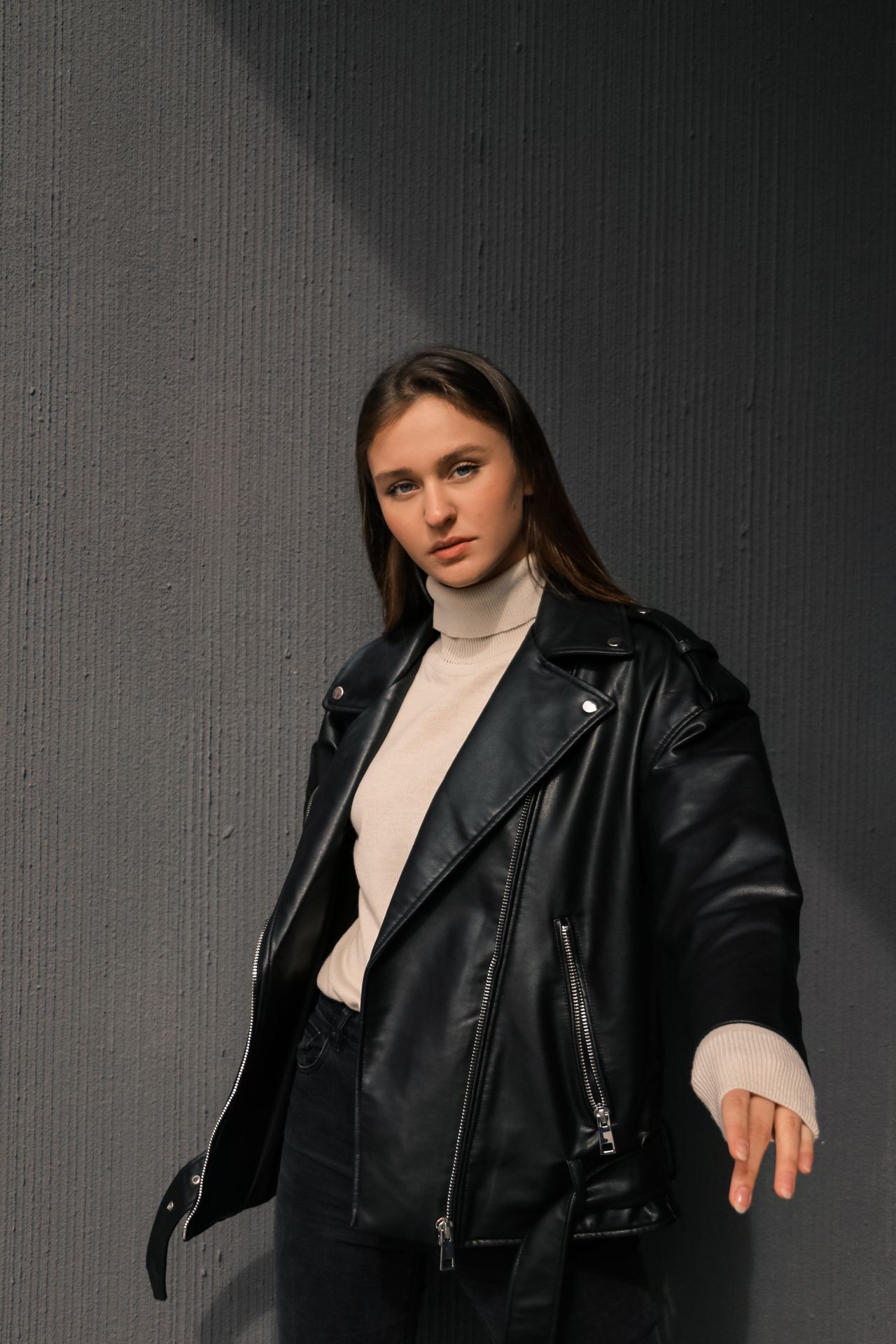 Woman wearing a black leather moto jacket over a white turtleneck sweater with dark jeans
