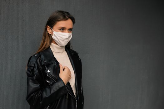 一名穿着皮夹克、戴着口罩的女人，倚靠在纹理墙壁上的肖像