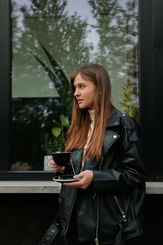 一位穿着黑色皮夹克的时尚女士正在户外享用咖啡