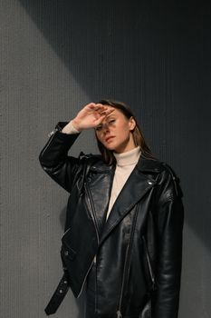 一位时尚女子穿着黑色皮夹克，靠在混凝土墙上，摆出戏剧性的光影姿势