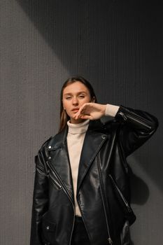 Caucasian woman in leather jacket posing stylishly indoors with dramatic shadows.