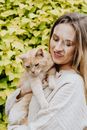 绿叶背景前，一位微笑的女人抱着家猫