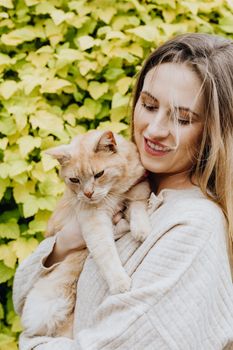 绿叶背景前，一位微笑的女人抱着家猫