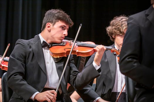 A violinist in a black suit performs passionately during an orchestra concert indoors.