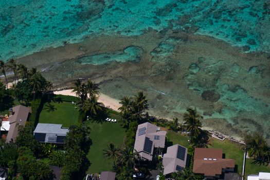 Stunning aerial shot of homes with solar panels by the turquoise coast and palm trees.