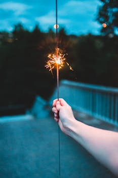 A person's hand holding a lit sparkler at twilight, creating a festive and magical atmosphere.