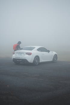 Back view of anonymous tourist with rucksack near contemporary auto on roadway under foggy sky