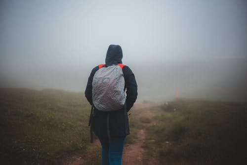 Unrecognizable tourist with rucksack walking on shabby path in fog