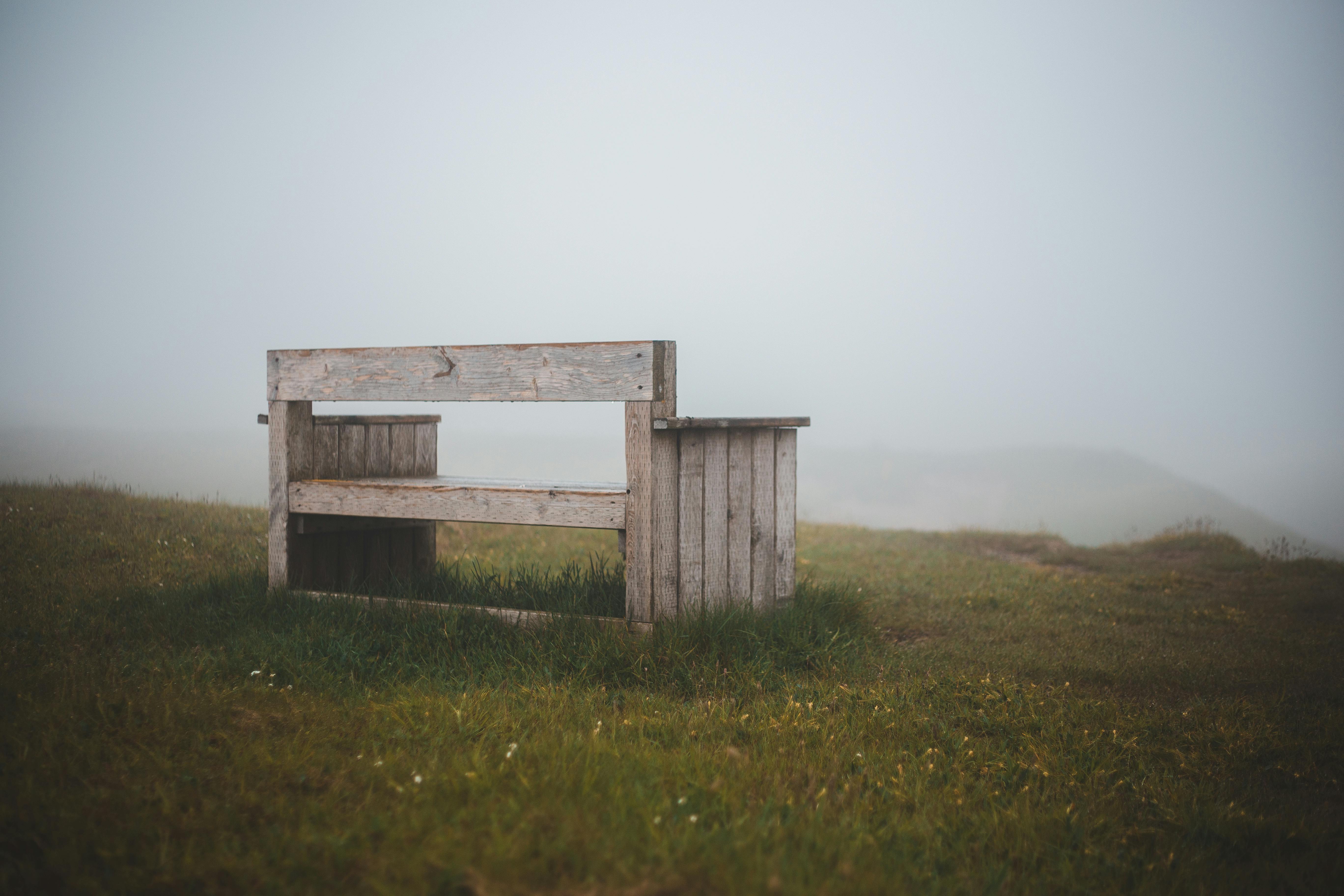雾蒙蒙的山上，日光下的绿色草坪旁，有一张古老的木凳
