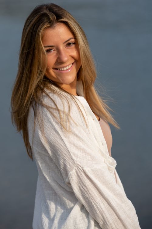 Free Positive female in white shirt smiling and looking at camera while standing on embankment near calm river on blurred background Stock Photo