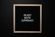 Top view of blackboard with written white REJECT WHITE SUPREMACY words on center on black background