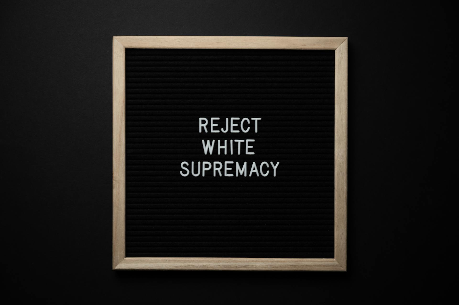 Top view of blackboard with written white REJECT WHITE SUPREMACY words on center on black background