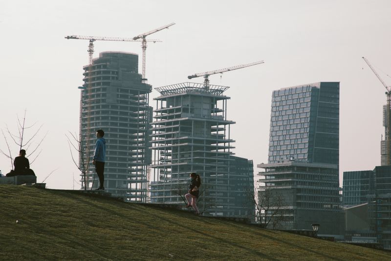 Urban skyline with construction cranes and people on a grassy hill in Shanghai, China.