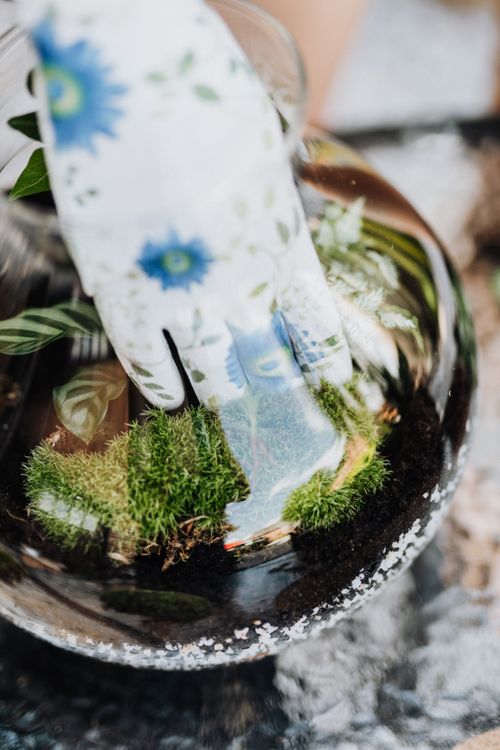 Free Close-up of a floral gardening glove arranging moss and plants in a glass terrarium. Stock Photo