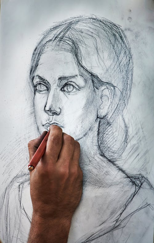 Free Crop unrecognizable person drawing portrait of charming woman with pencil on canvas in art studio Stock Photo