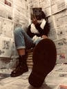 Woman Sitting in Corner Covered in Newspaper Pages Reading Book