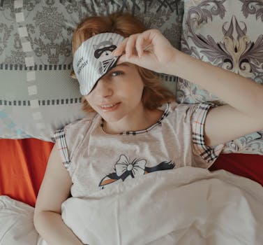 Woman waking up comfortably in bed, wearing a cute sleep mask in the morning.